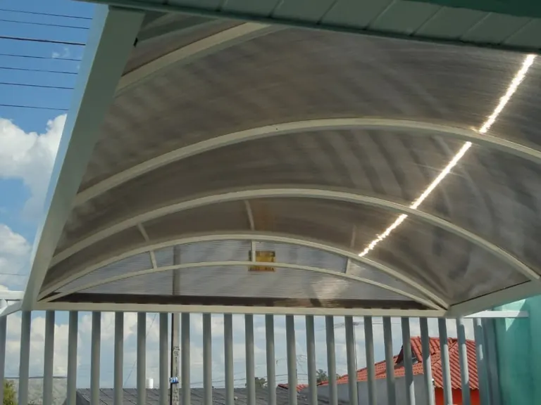 Vista inferior de cobertura curva de policarbonato instalada sobre varanda com guarda-corpo